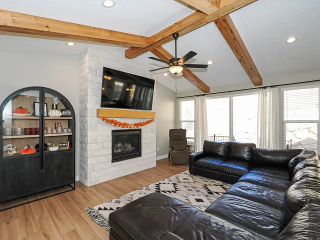 Living area featuring a floor-to-ceiling brick fireplace with a wood mantle, vaulted ceiling with exposed wood beams, recessed lighting, and wood-finish flooring