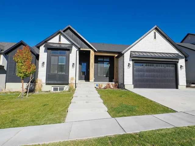 Modern farmhouse exterior featuring black board-and-batten siding with white shingle accents, a dark gray garage door, and a concrete walkway