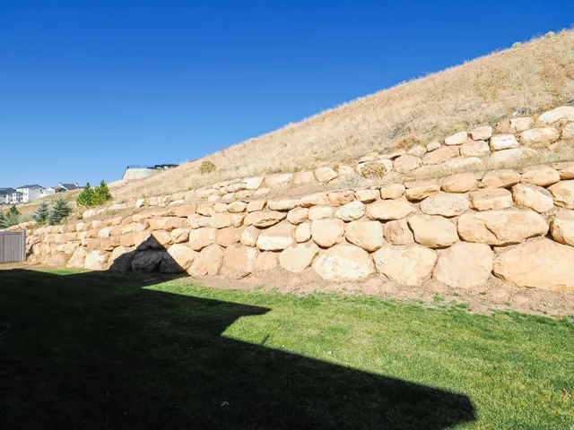 Expansive backyard featuring a stone retaining wall, grassy lawn, and natural hillside landscaping