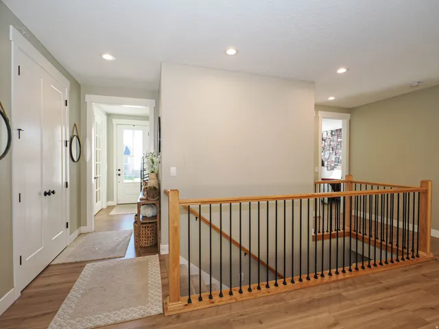 Spacious hallway with light wood-finish flooring, recessed lighting, and a contemporary wood and metal stair railing