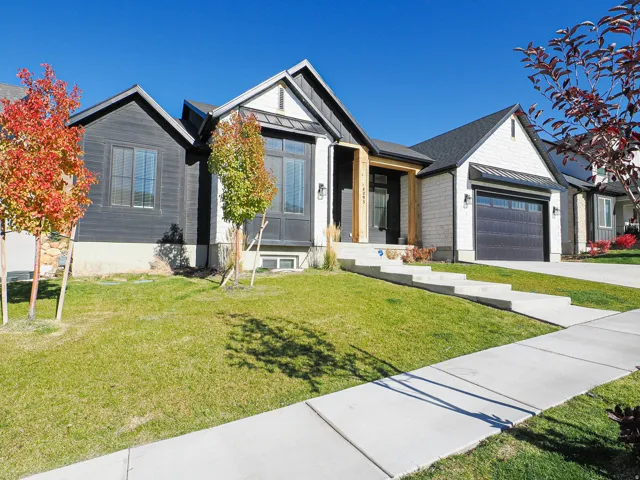 Modern home exterior featuring dark horizontal siding, white vertical siding, a deep blue garage door with window inserts, a covered entry with wood-finish columns, and a concrete walkway