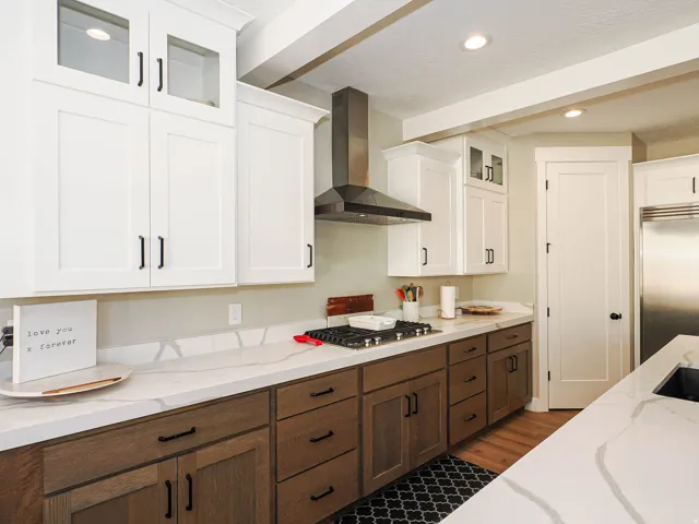 Modern kitchen featuring white upper cabinetry with glass inserts, wood-finish lower cabinetry, and extensive light-toned countertops with veining