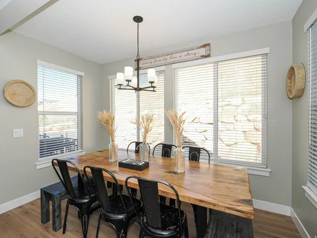 Dining area featuring a wood-finish table, a five-light chandelier with white glass shades, and multiple windows with horizontal blinds