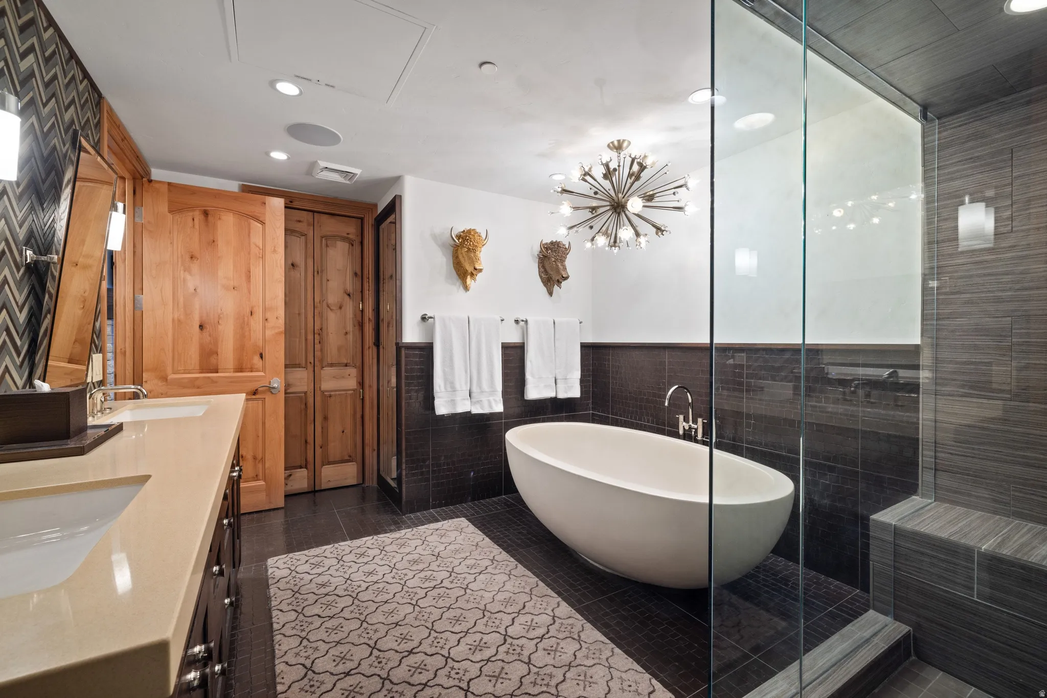 Contemporary bathroom featuring a freestanding soaking tub, glass-enclosed shower with tiled bench, dual vanity with undermount sinks and light-toned countertops, and wood-panel doors