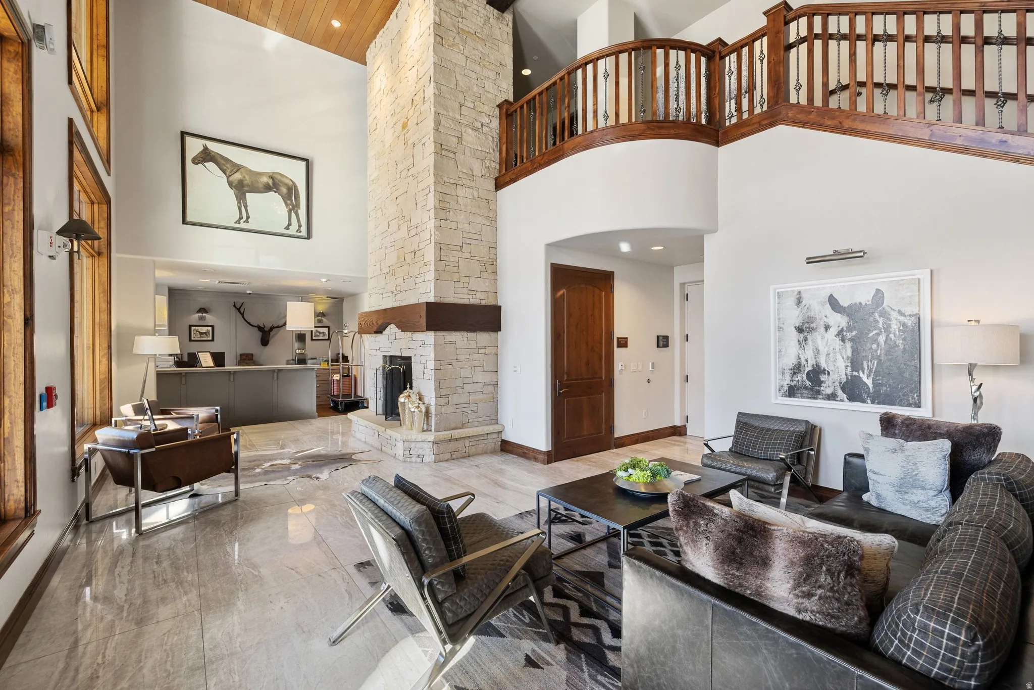 Open-concept living space featuring a two-story stone-faced fireplace, vaulted wood-plank ceiling, and polished stone flooring
