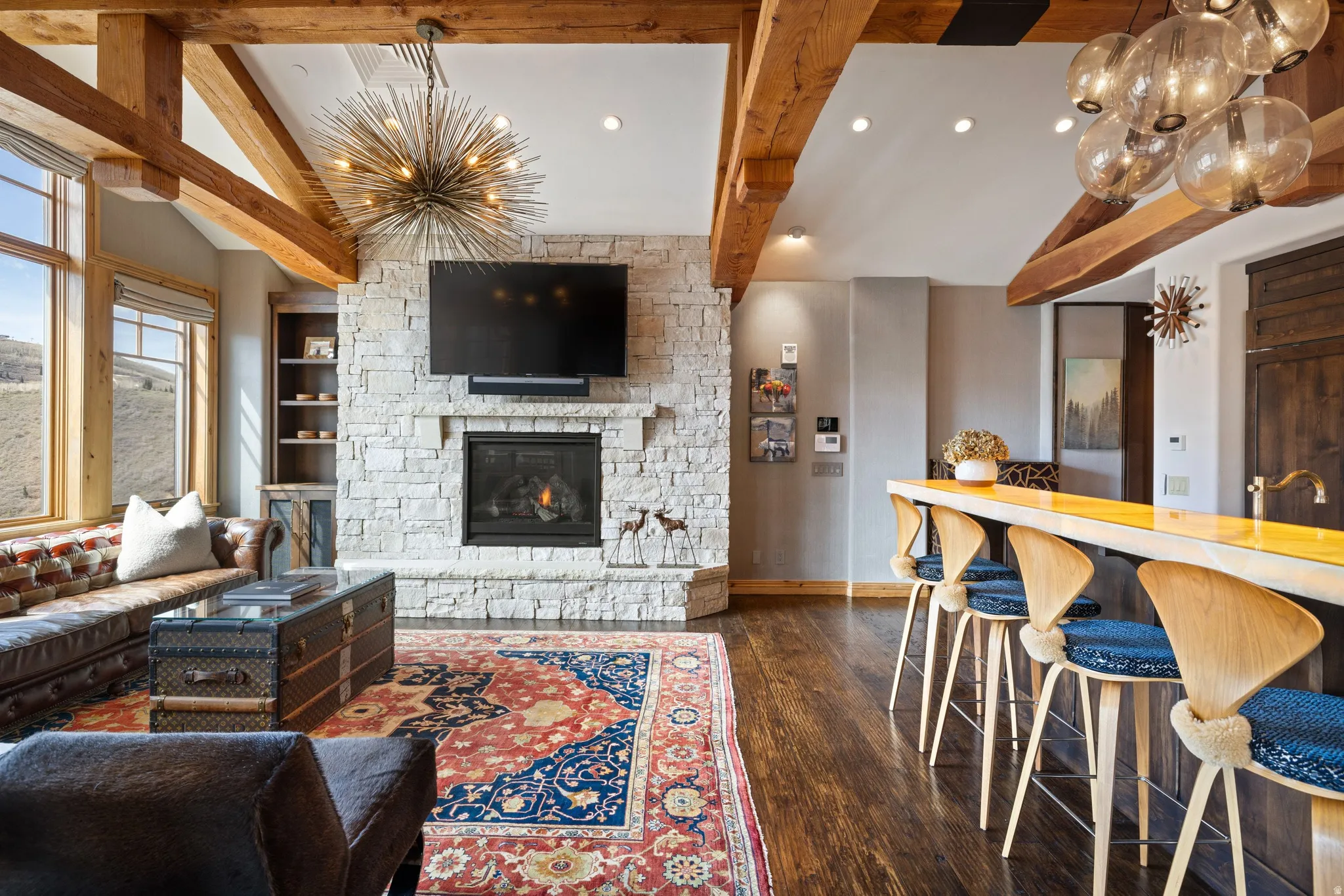 Great room featuring exposed wood beams, a stone-clad fireplace, and wood-finish flooring