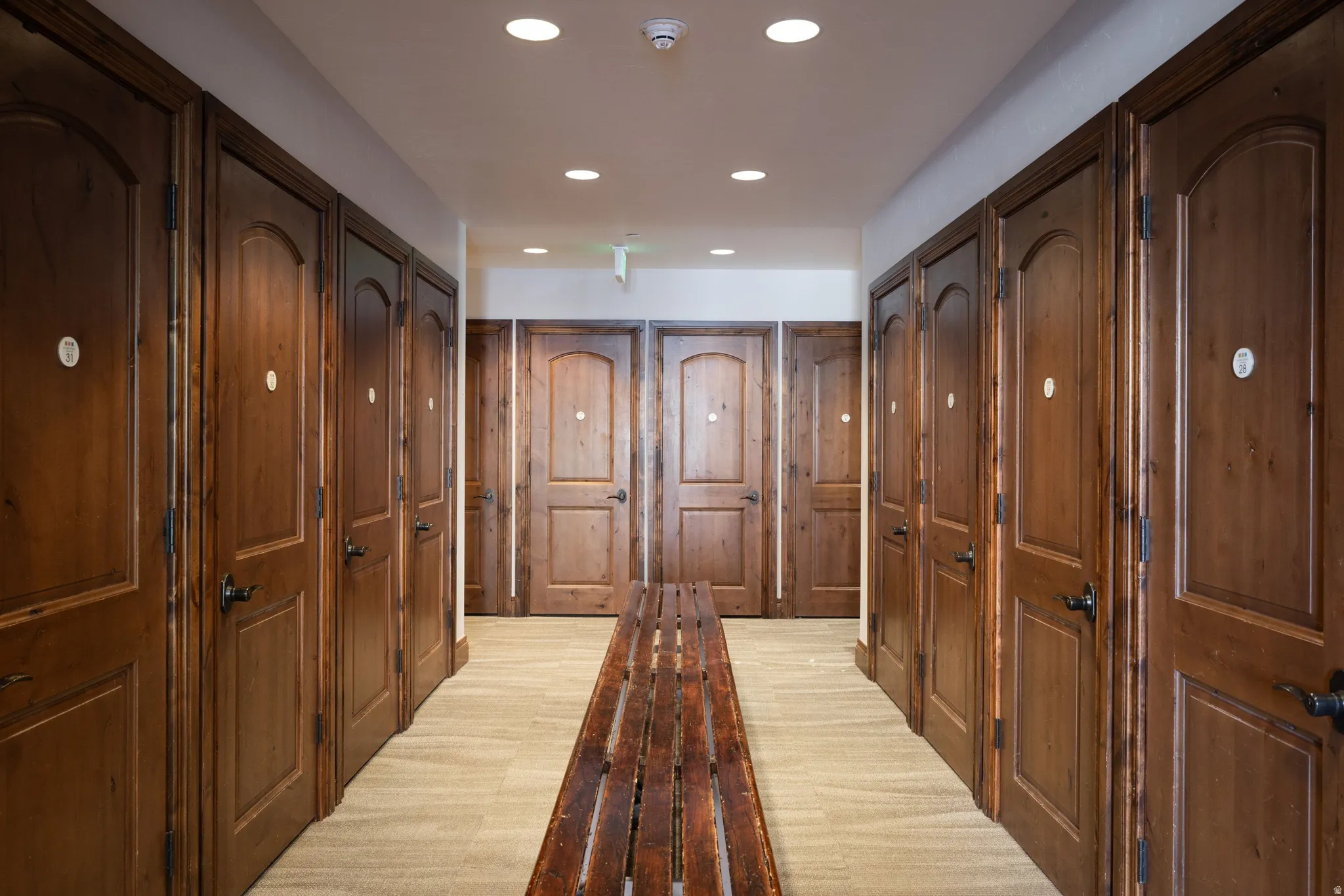 Hallway featuring recessed lighting, carpeted flooring, and a series of wood-paneled doors with dark hardware