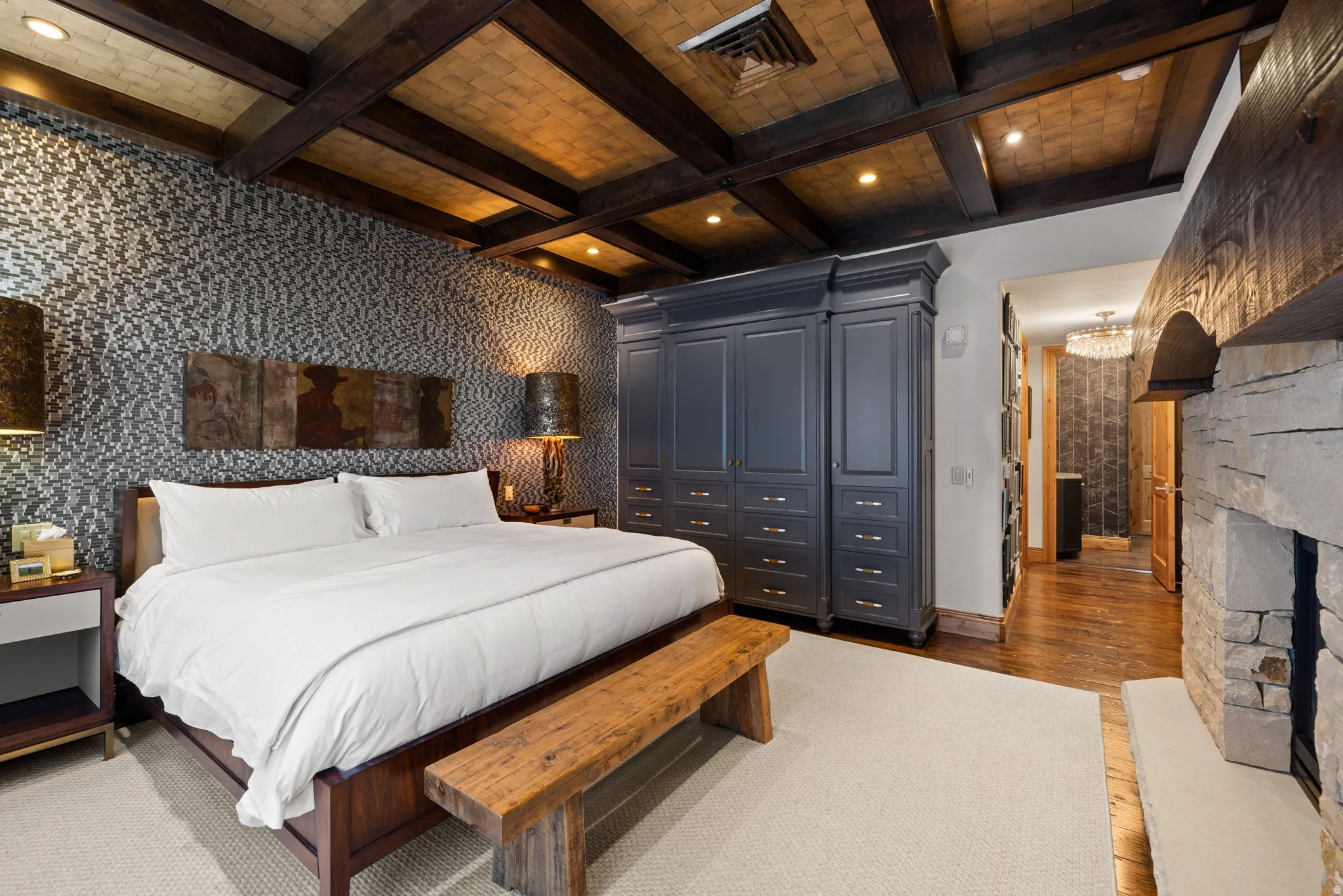 Textured accent wall, coffered wood-beam ceiling, built-in cabinetry, stone fireplace, and wood-finish flooring