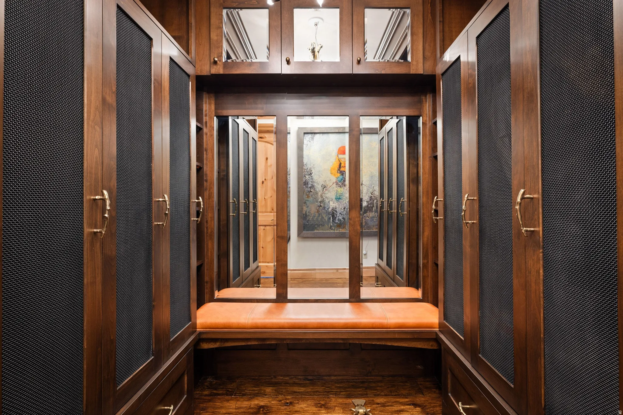 Custom wood cabinetry with perforated panel doors, an integrated cushioned bench, brass hardware, and wood-finish flooring