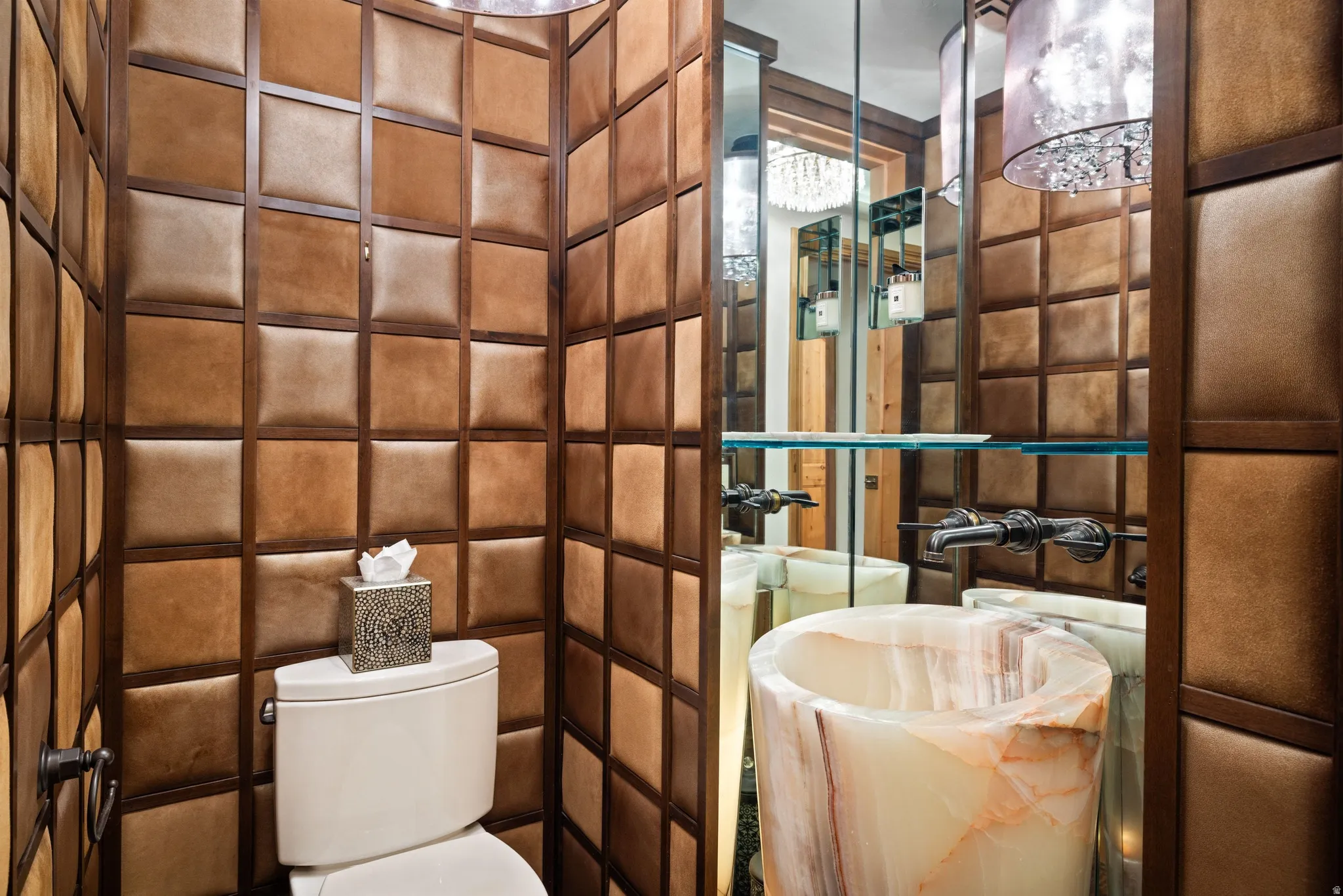 Powder room featuring padded wall panels with wood trim, an onyx pedestal sink, wall-mounted faucet, and a decorative pendant light fixture