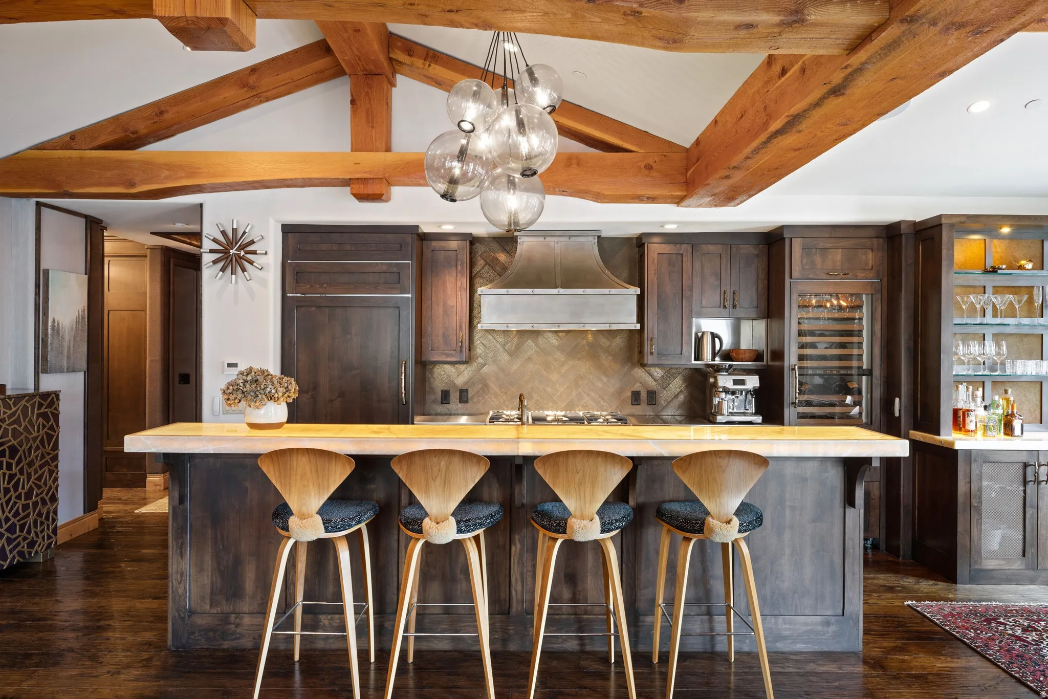 Gourmet kitchen featuring exposed wood beams, a spacious island with seating, dark wood cabinetry, stainless steel range hood, and a built-in wine cooler