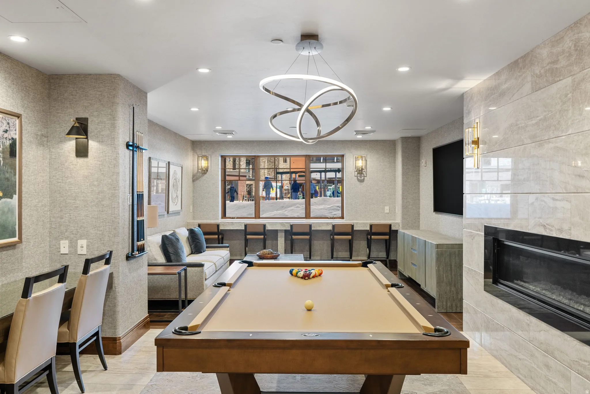 Recreation room featuring a prominent billiards table, a contemporary linear chandelier, a built-in fireplace with a tiled surround, a window bar with barstools, and recessed lighting