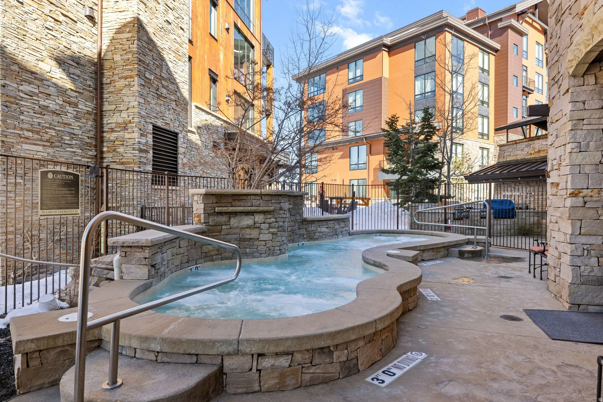 Stone-clad outdoor spa with integrated waterfall feature and stainless steel handrails