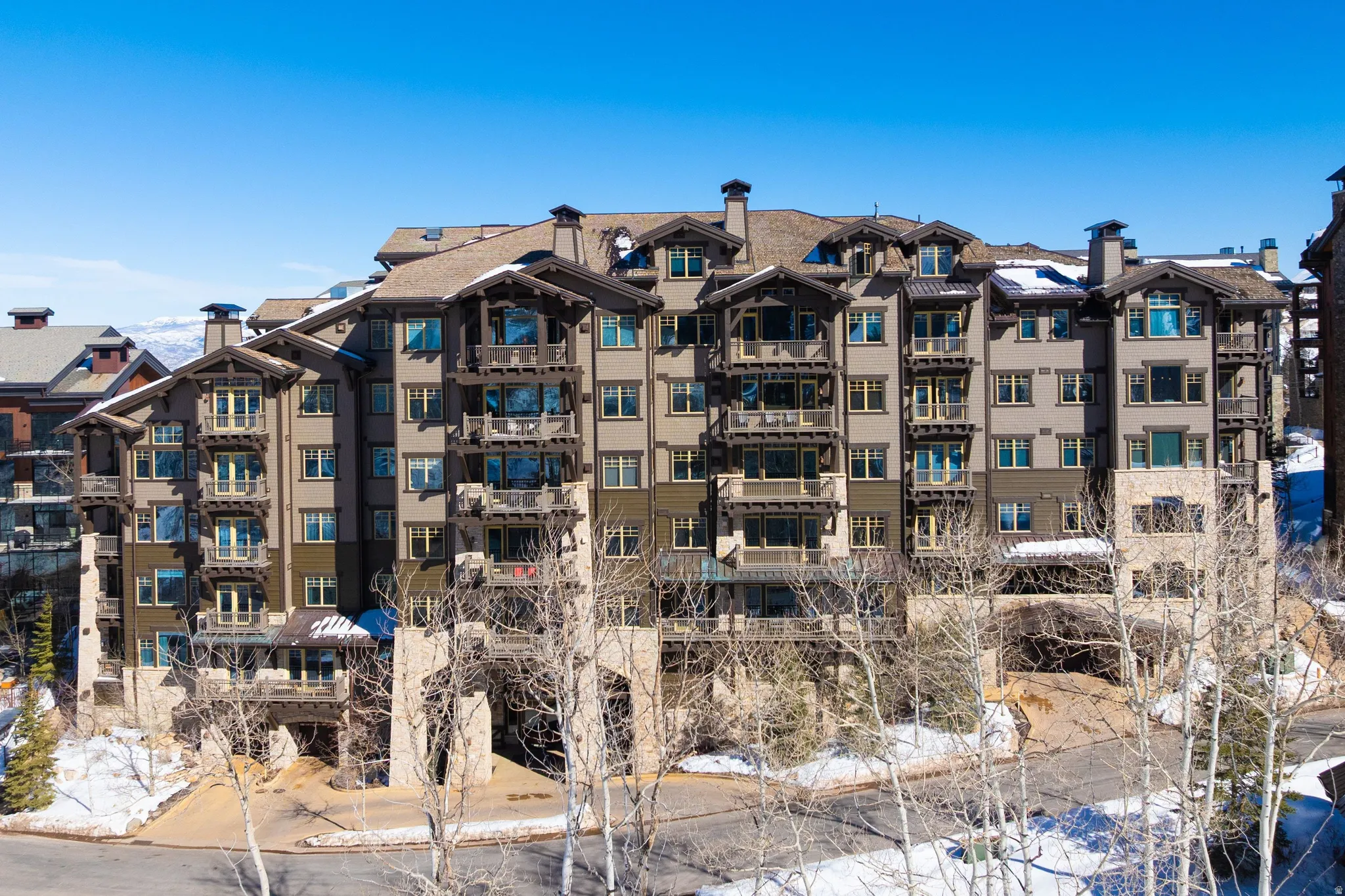 Multi-story residential building featuring extensive balconies, stone and stucco exterior, prominent timber architectural details, and a multi-gabled roofline