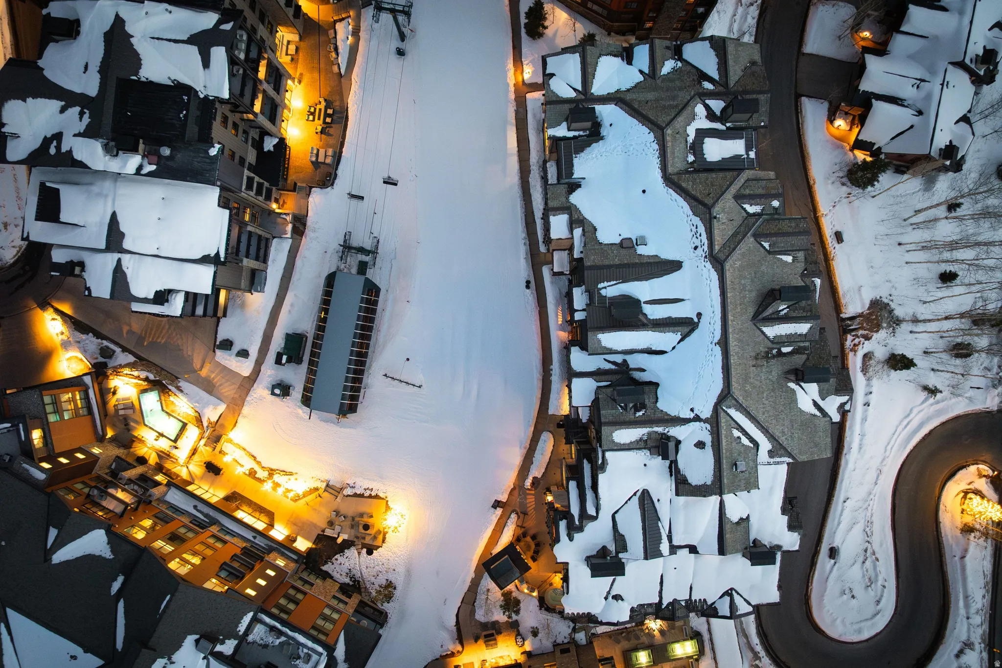 Extensive resort grounds featuring multiple buildings with illuminated windows, a ski lift structure, and winding roads