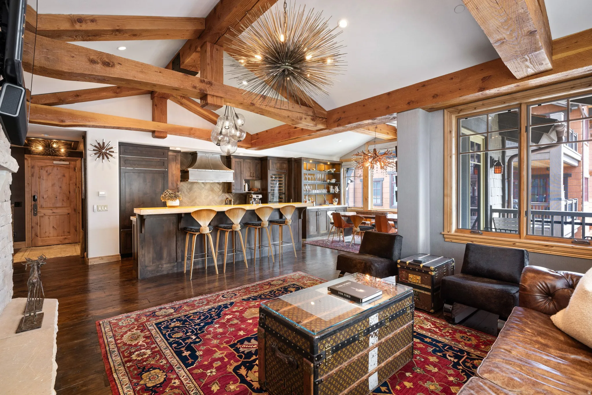 Spacious living area featuring exposed wood beams, wood-finish flooring, a stone fireplace, and large multi-pane windows