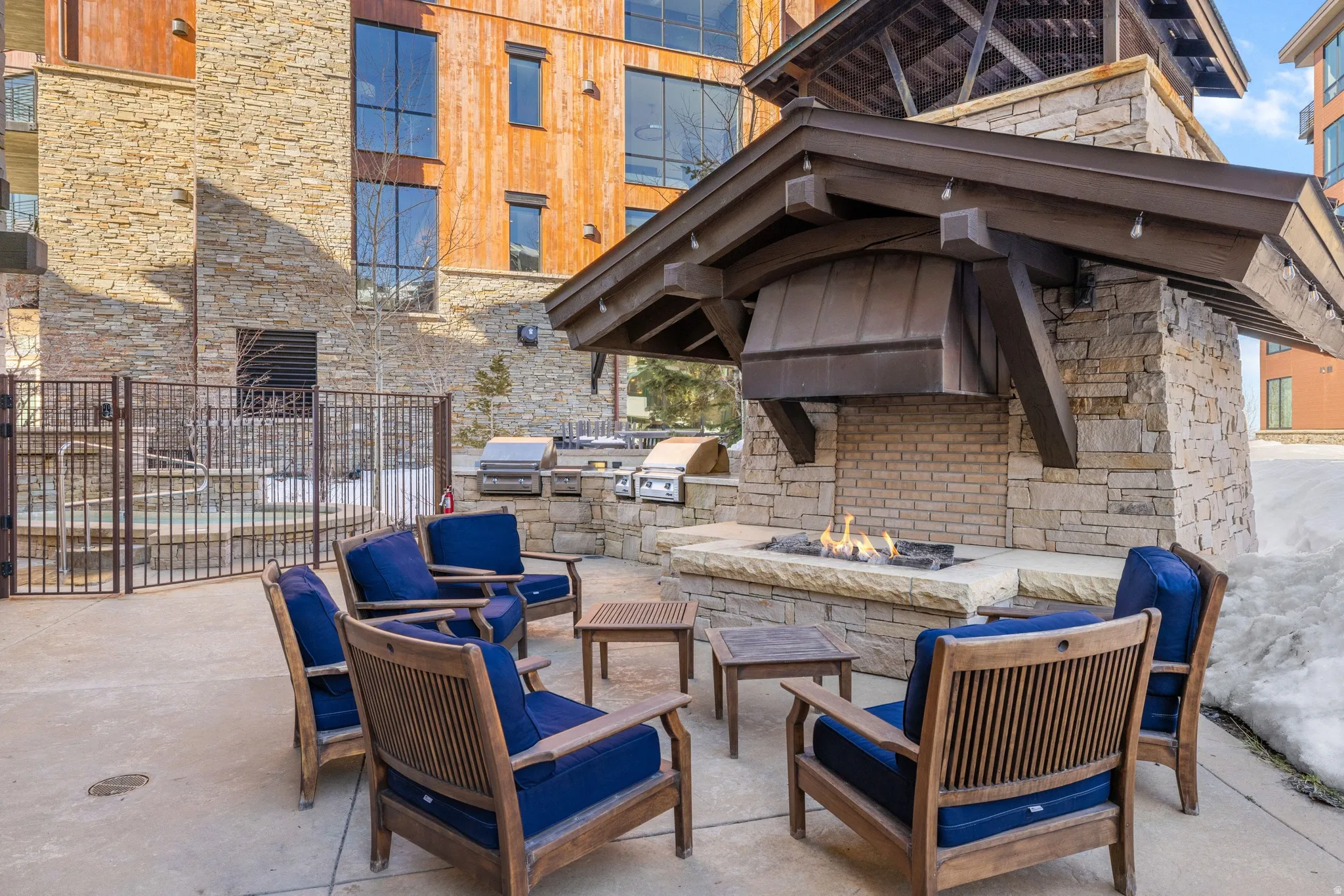 Outdoor patio featuring a stone fireplace with a metal hood, multiple barbecue grills, and a fenced spa