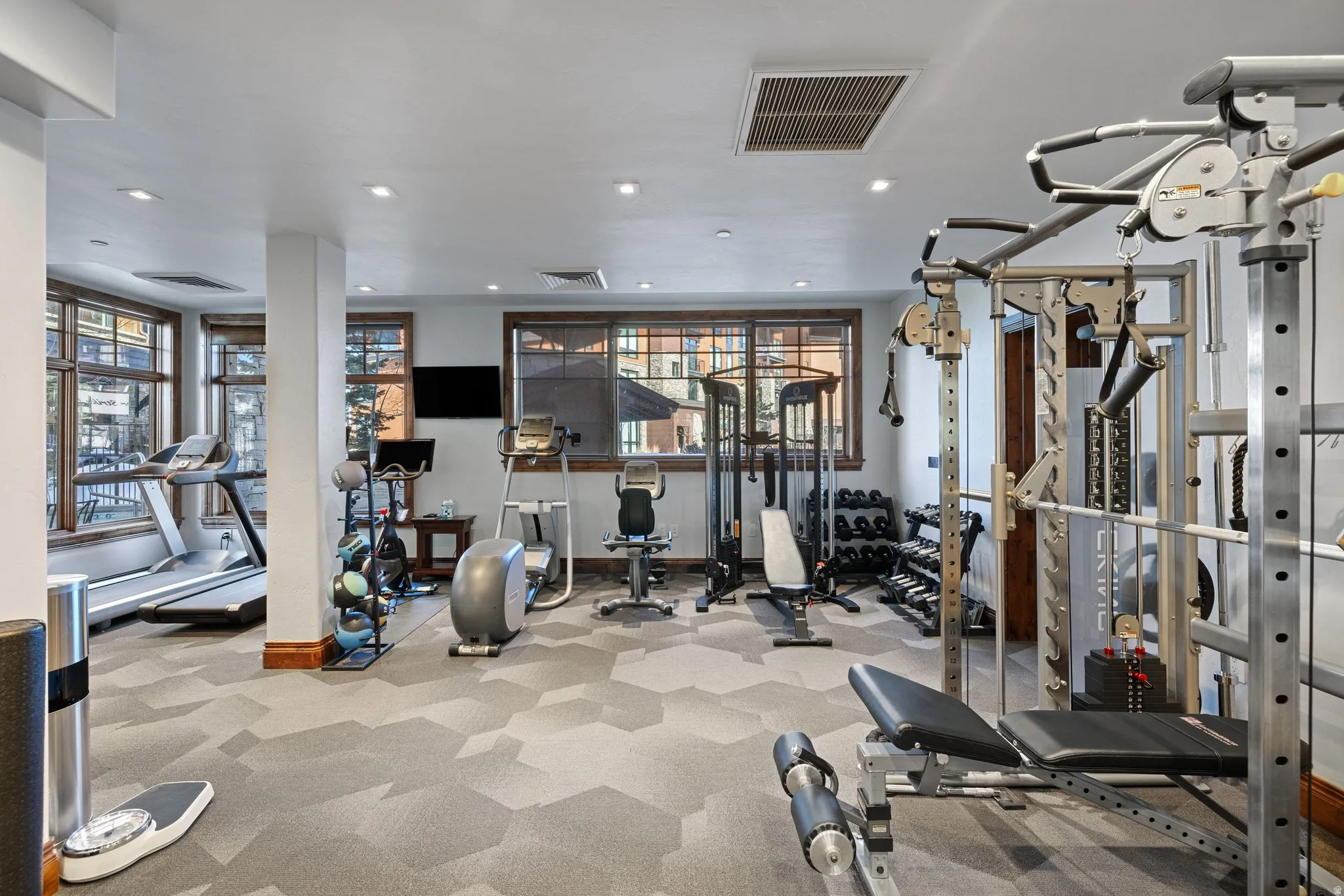 Dedicated fitness room featuring patterned carpeting, recessed lighting, and large windows with wood trim