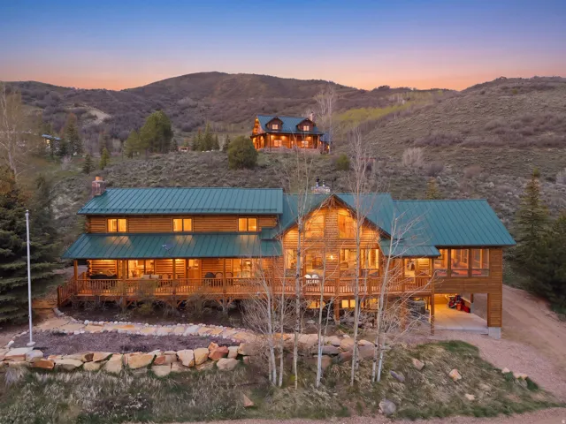 Log cabin exterior with a green metal roof, multiple windows, and an extensive wraparound porch