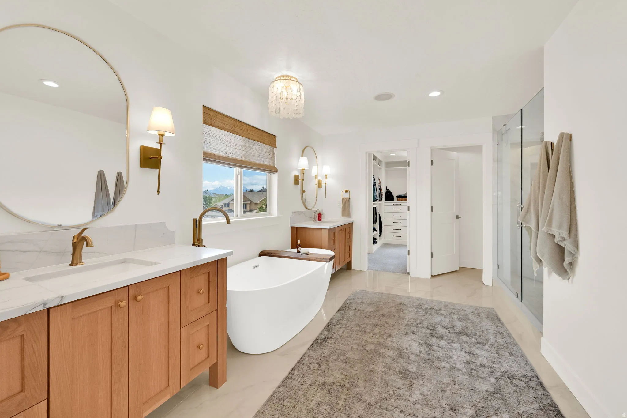 Bright bathroom featuring a freestanding soaking tub, dual vanity with light wood cabinetry and white countertops, a walk-in shower with glass enclosure, and direct access to a custom closet