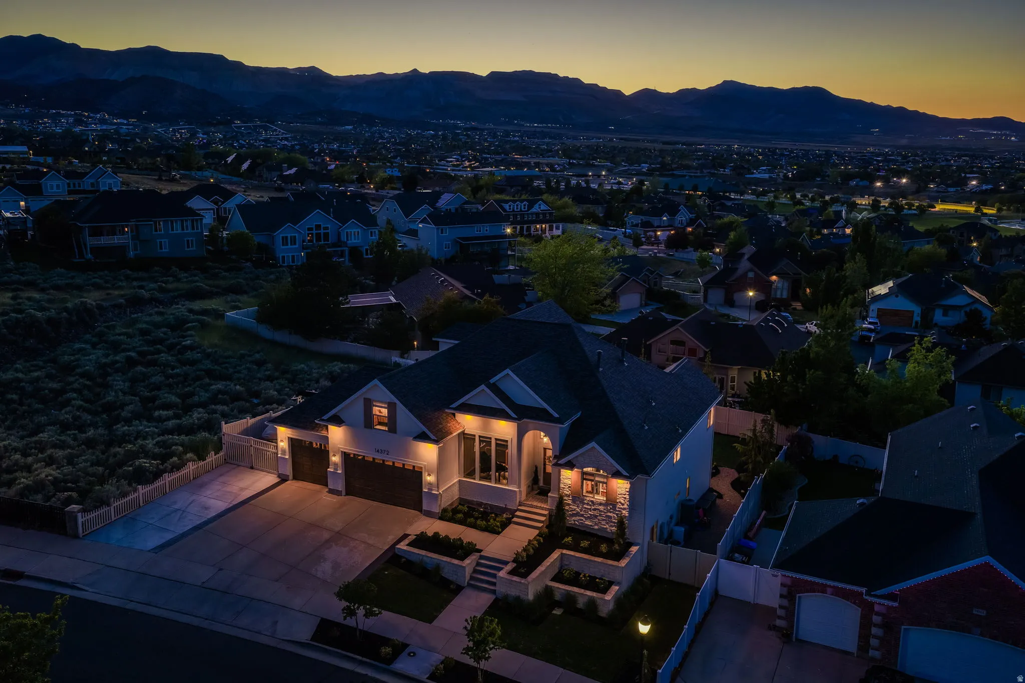 Contemporary residence featuring an illuminated facade, multi-level landscaping, and a three-car garage