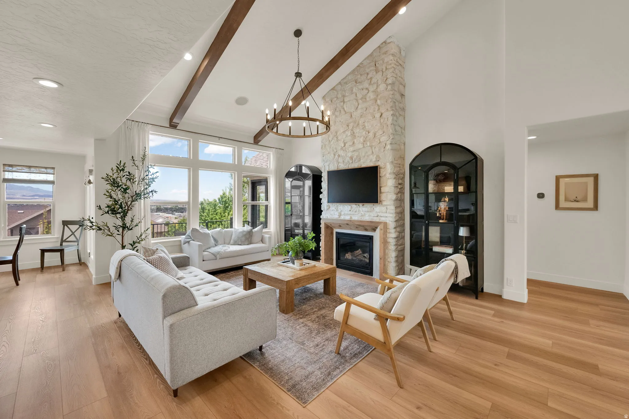 Spacious living area featuring high vaulted ceilings with exposed wood beams, a stone-clad fireplace with wood mantle, large picture windows, and wood-finish flooring
