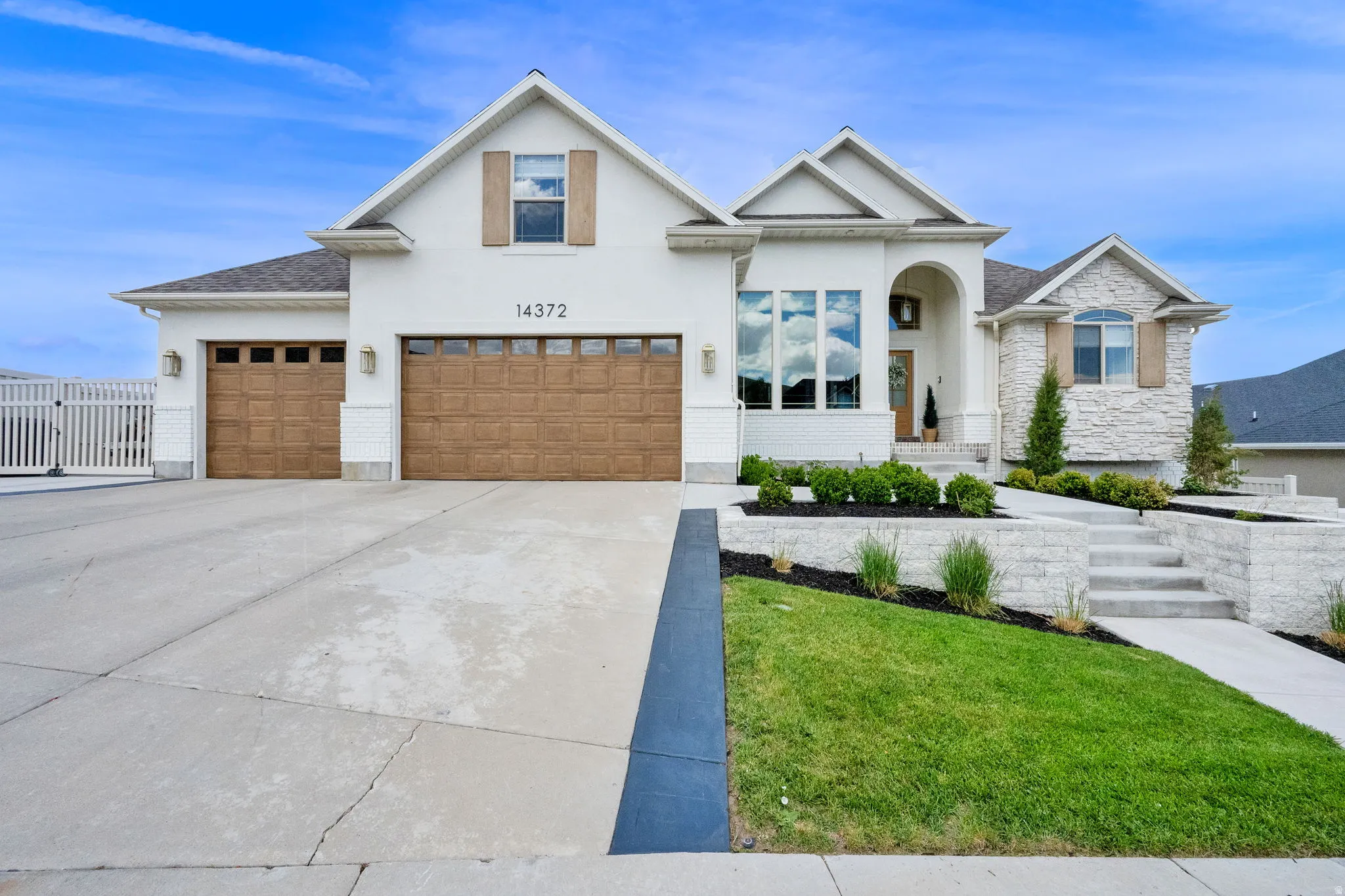 Contemporary stucco and stone exterior featuring a two-car garage with wood-finish doors