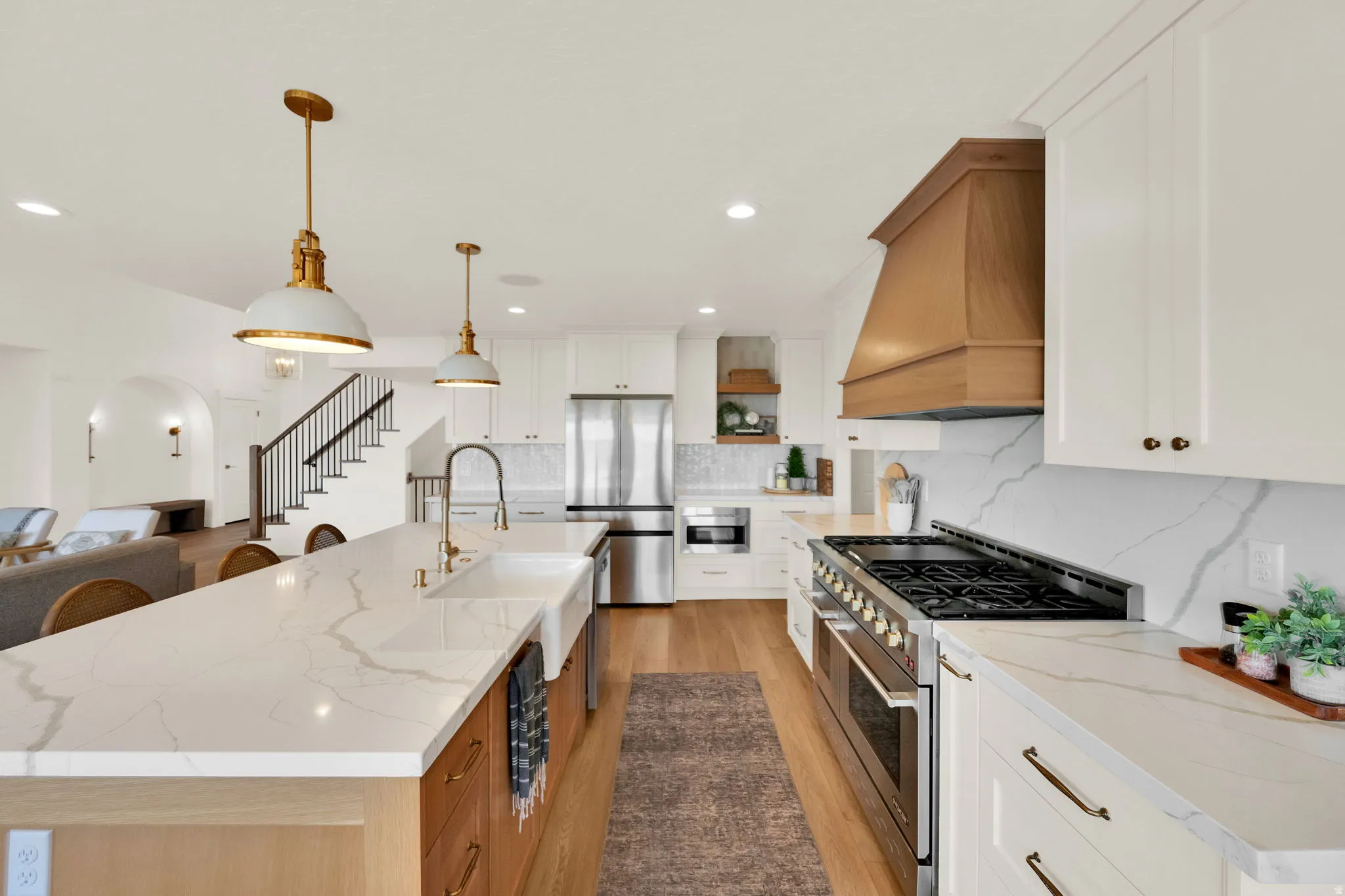 Gourmet kitchen with wood-finish flooring, white cabinetry, integrated stainless steel appliances, and a substantial center island featuring a farmhouse sink