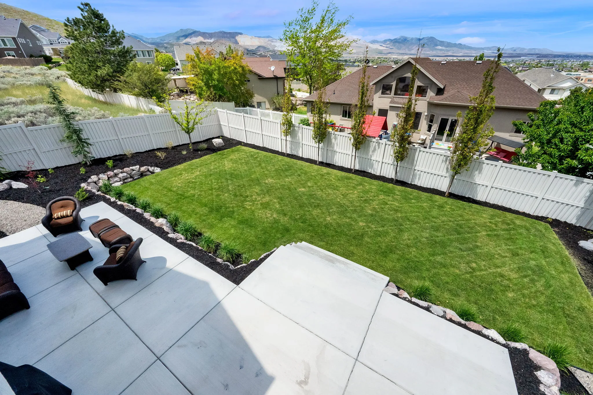 Expansive backyard featuring a large concrete patio, manicured lawn, and a white privacy fence