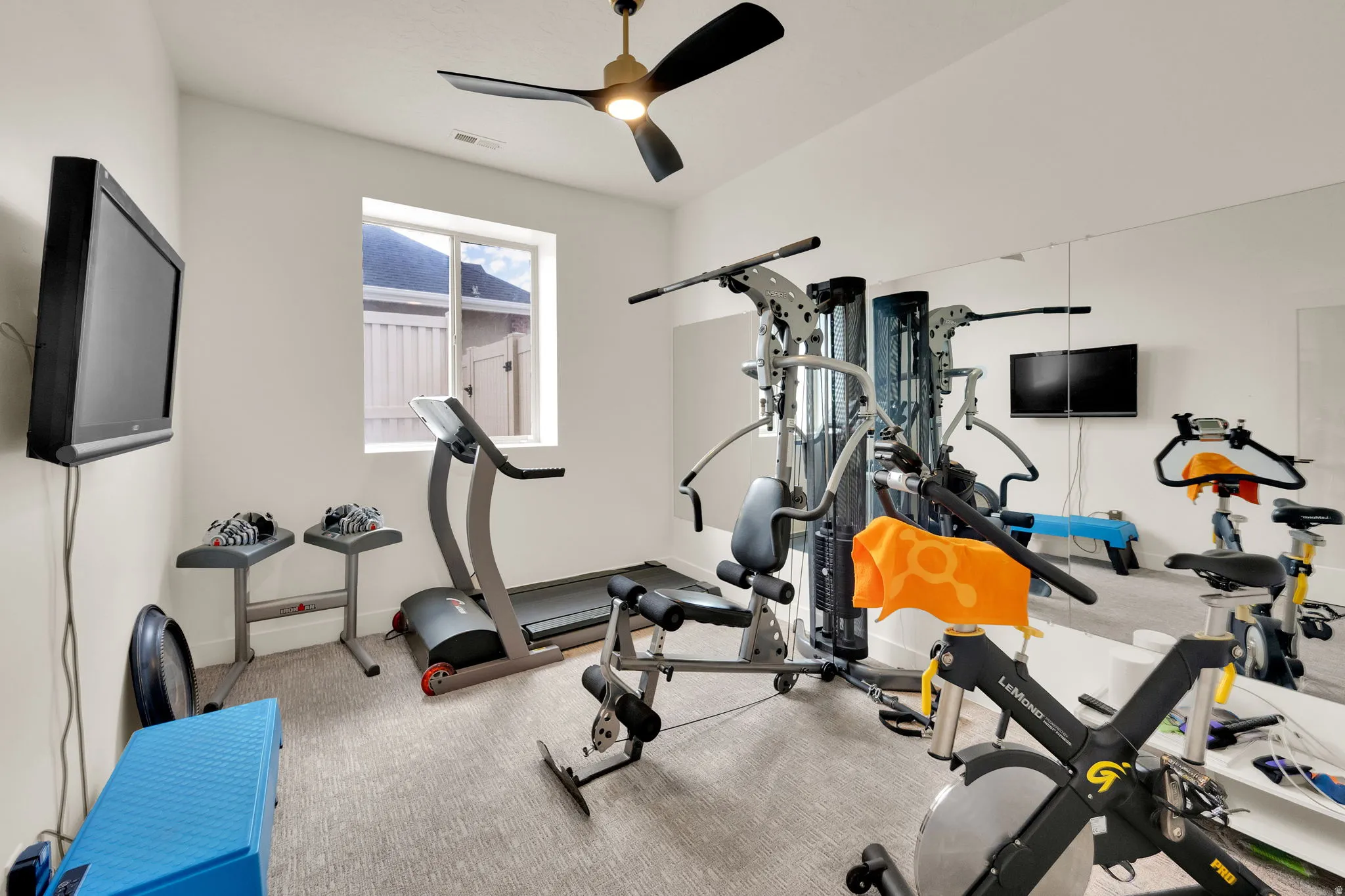 Dedicated exercise room featuring a ceiling fan, light neutral walls, and a window