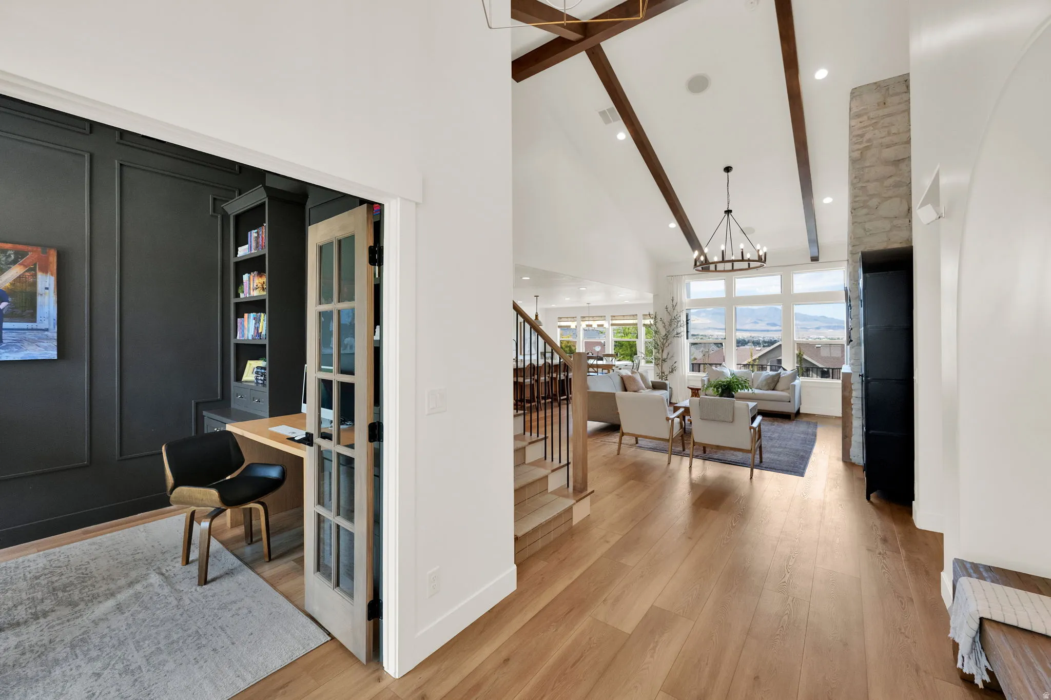 Entryway featuring wood-finish flooring, a dedicated office space with built-in shelving, glass-paned French doors, and an open-concept living area with vaulted ceilings and exposed wood beams