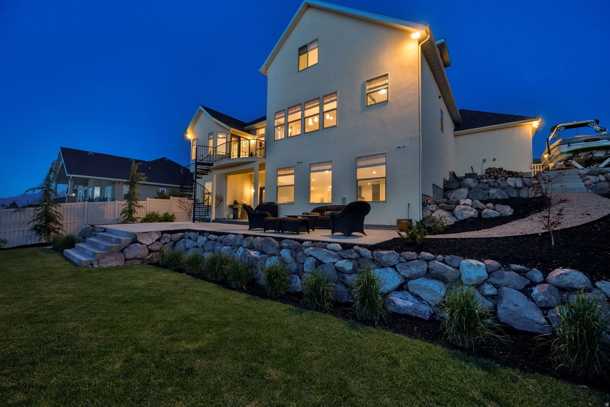 Rear facade featuring a concrete patio, spiral staircase, and tiered landscaping