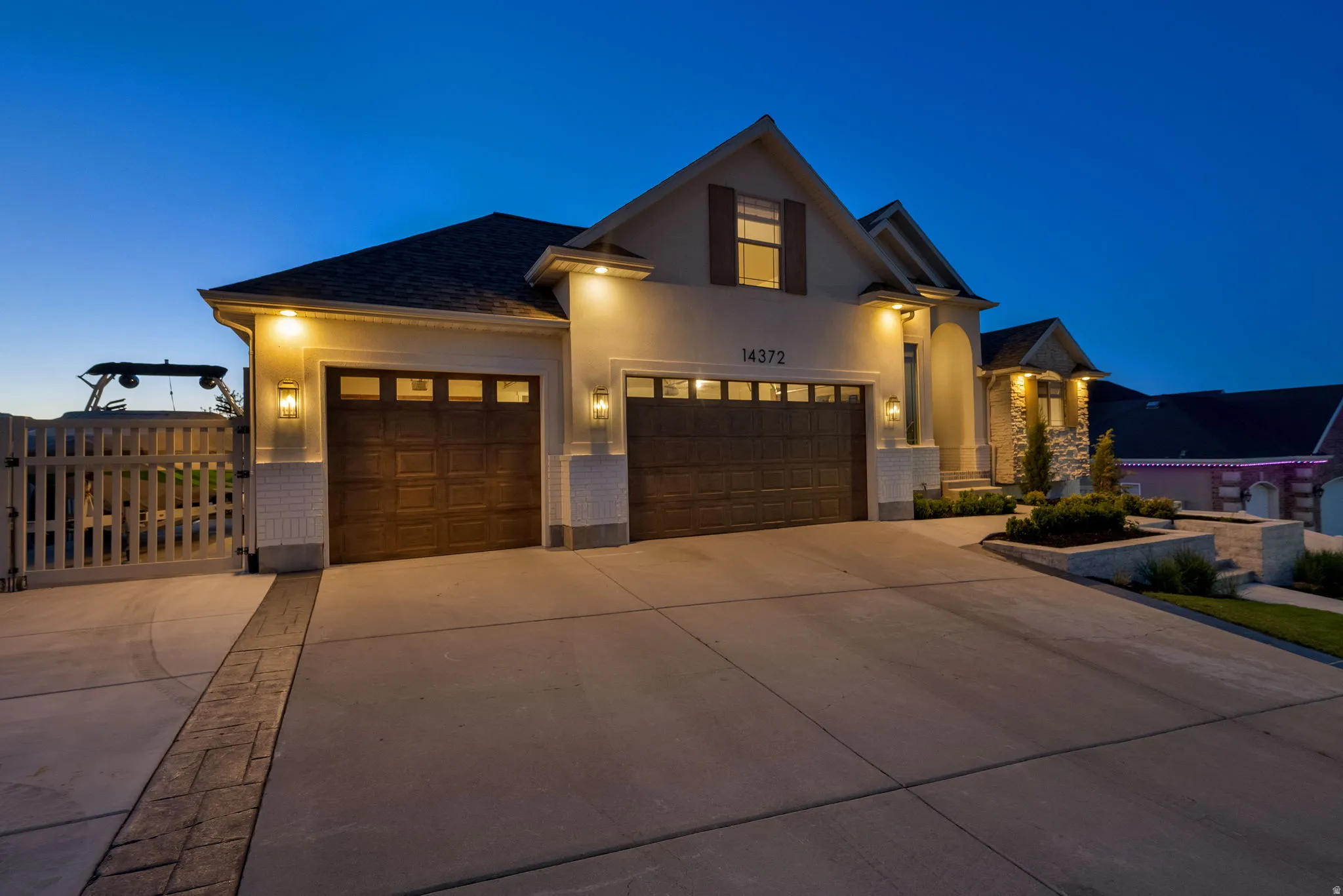 Stucco and stone exterior featuring multiple gables, a two-car garage with wood-finish doors, and integrated outdoor lighting