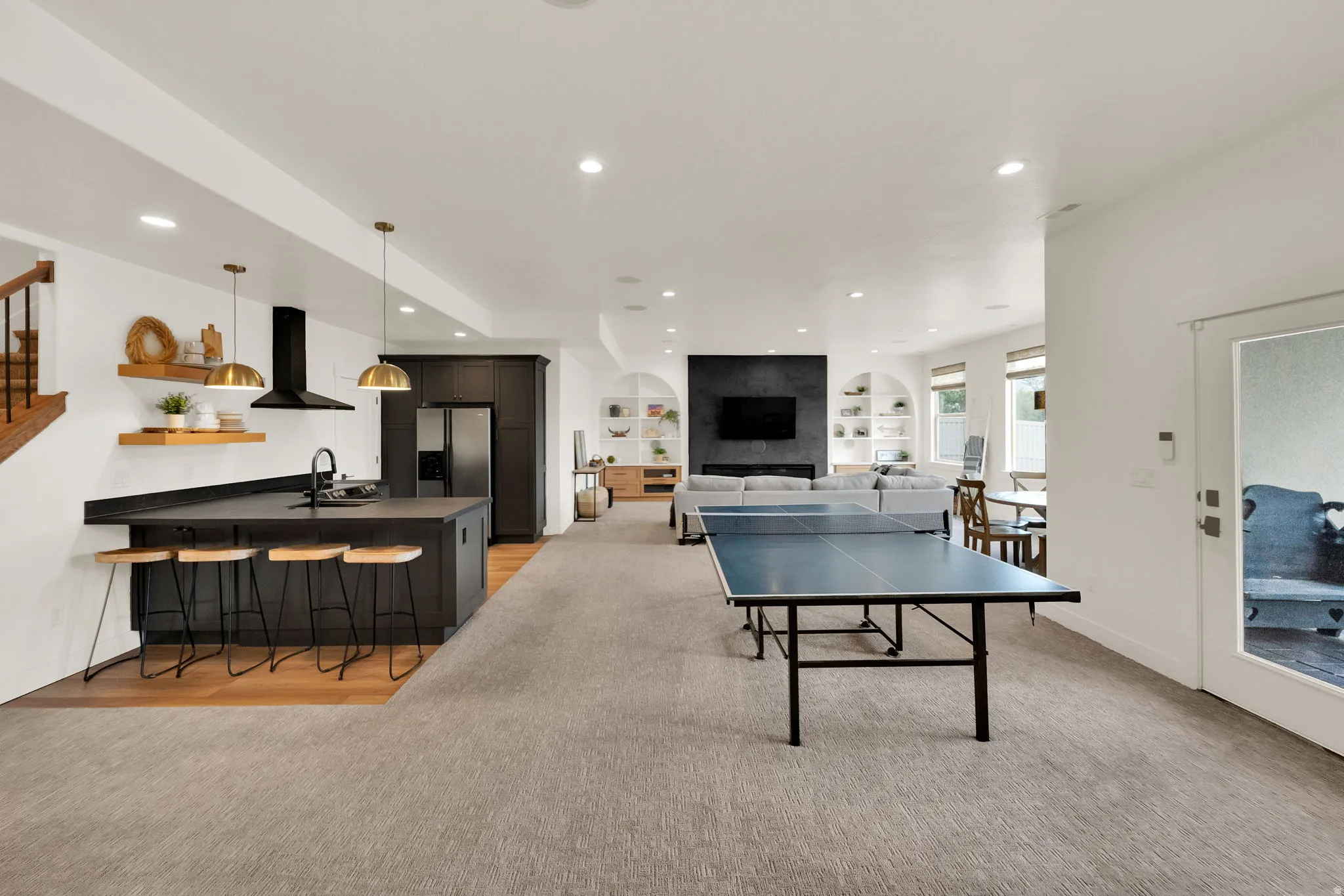 Open-concept recreation space with a full kitchen island, integrated appliances, recessed lighting, and built-in shelving