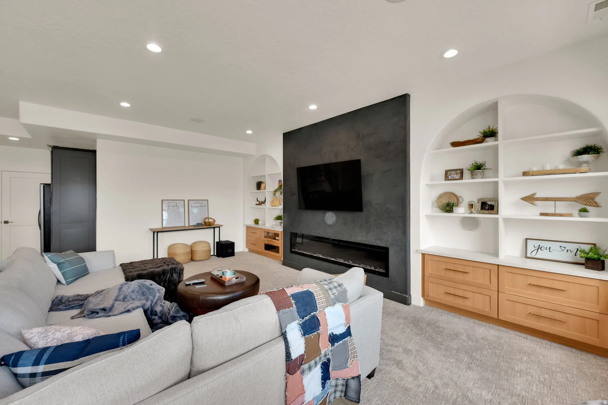 Spacious living area featuring a dark accent wall with a linear fireplace, built-in arched shelving, light wood-finish cabinetry, and recessed lighting