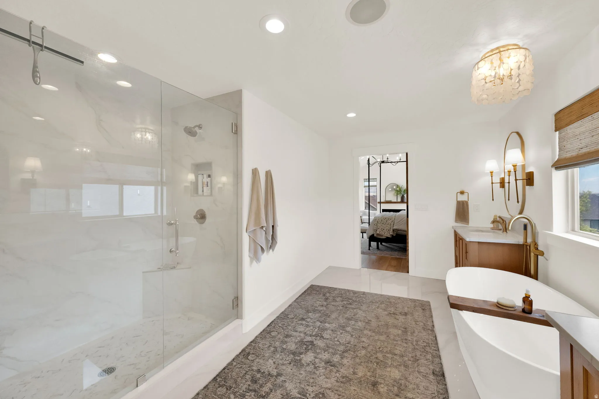 Spacious bathroom featuring a frameless glass shower enclosure, a freestanding soaking tub, a single vanity with a stone countertop, a gold-framed mirror, and recessed lighting