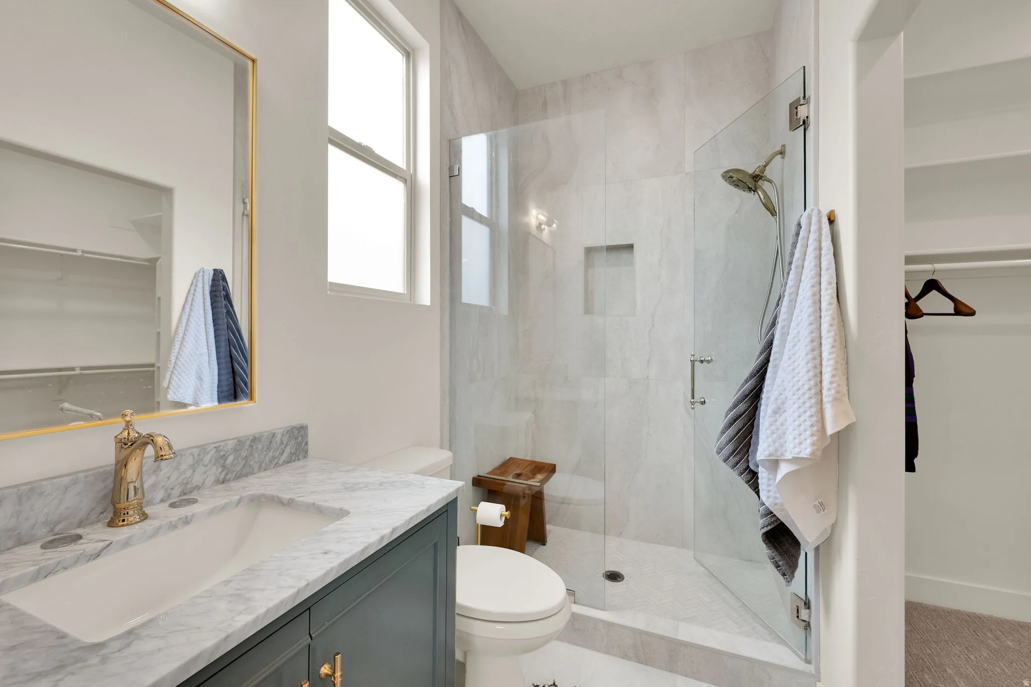 Bathroom featuring a walk-in shower with glass enclosure, single vanity with a marble countertop, gold-tone faucet, and an integrated rectangular sink