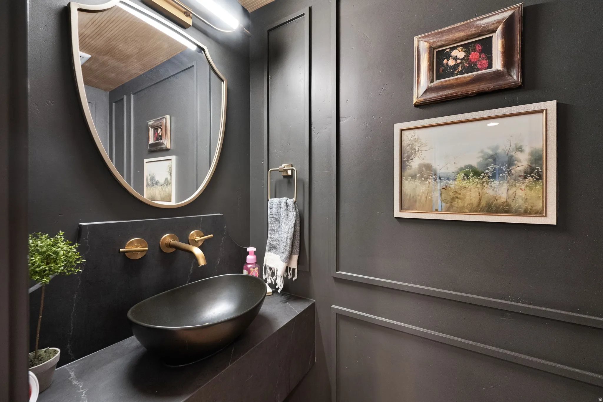 Powder room featuring a black vessel sink, wall-mounted bronze faucet, black stone countertop, and a decorative gold-framed mirror