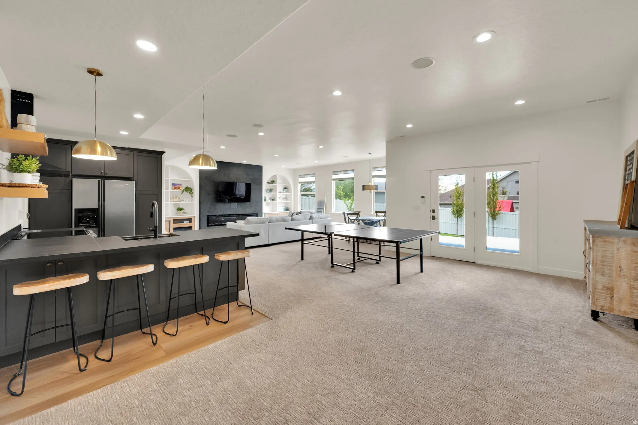 Open-concept living space featuring a full kitchen with dark cabinetry and stainless steel appliances, a large island with seating, recessed lighting, and double French doors opening to the exterior