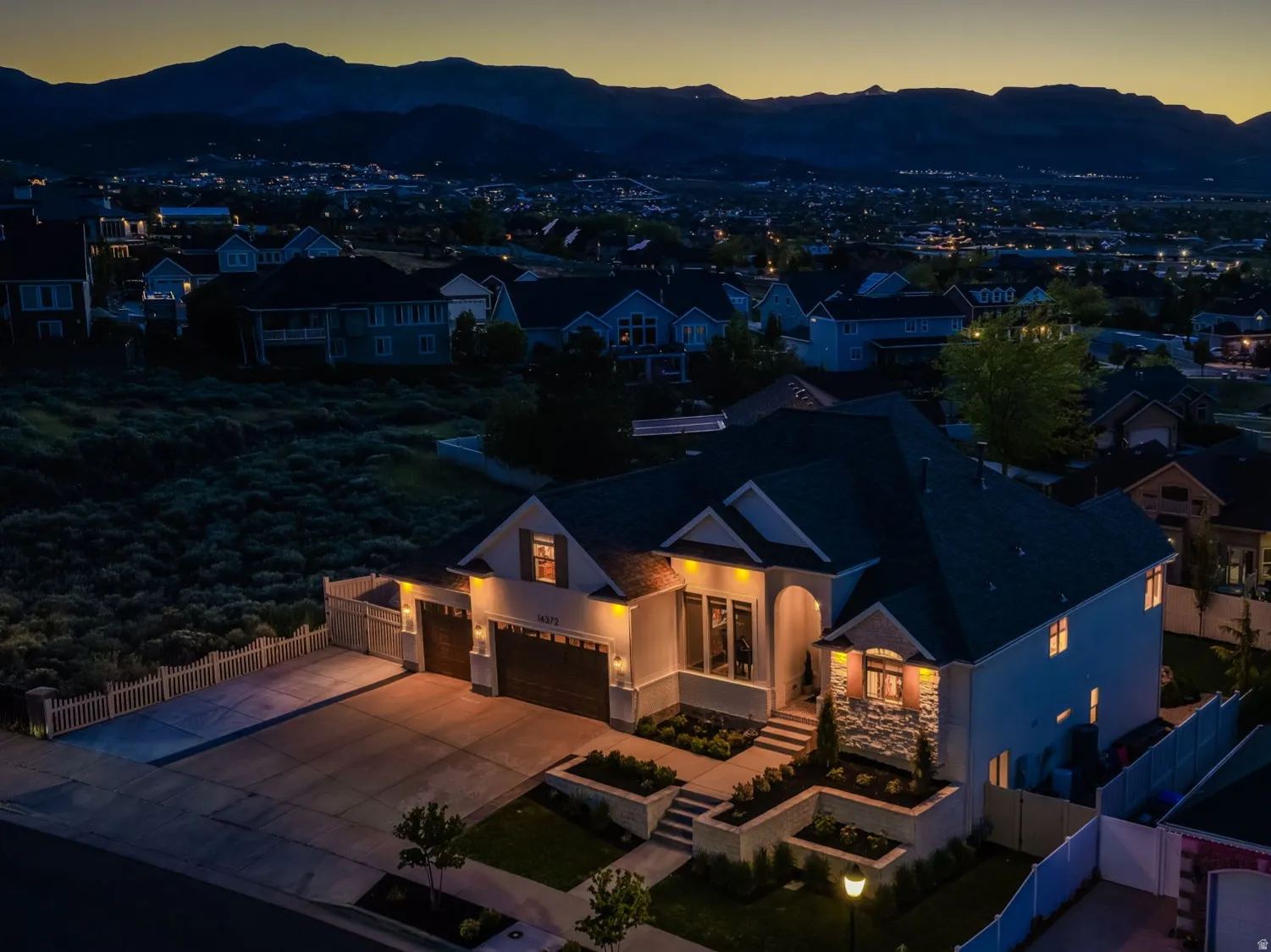 Contemporary residence featuring a stucco and stone facade, dark-toned roofing, and illuminated landscaping