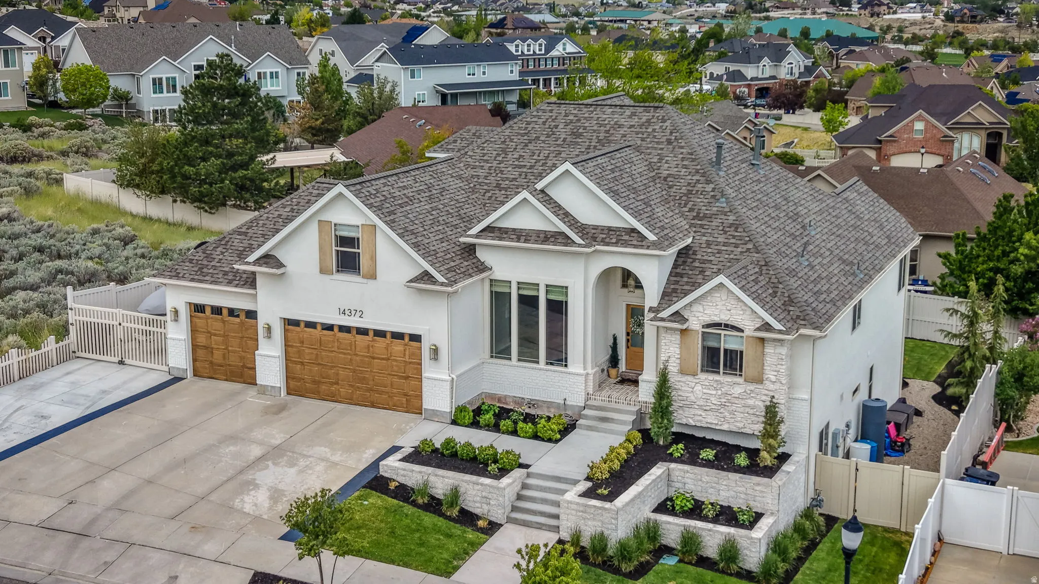 White stucco exterior with stone accents, a three-car garage featuring wood-finish doors, and a multi-level concrete walkway