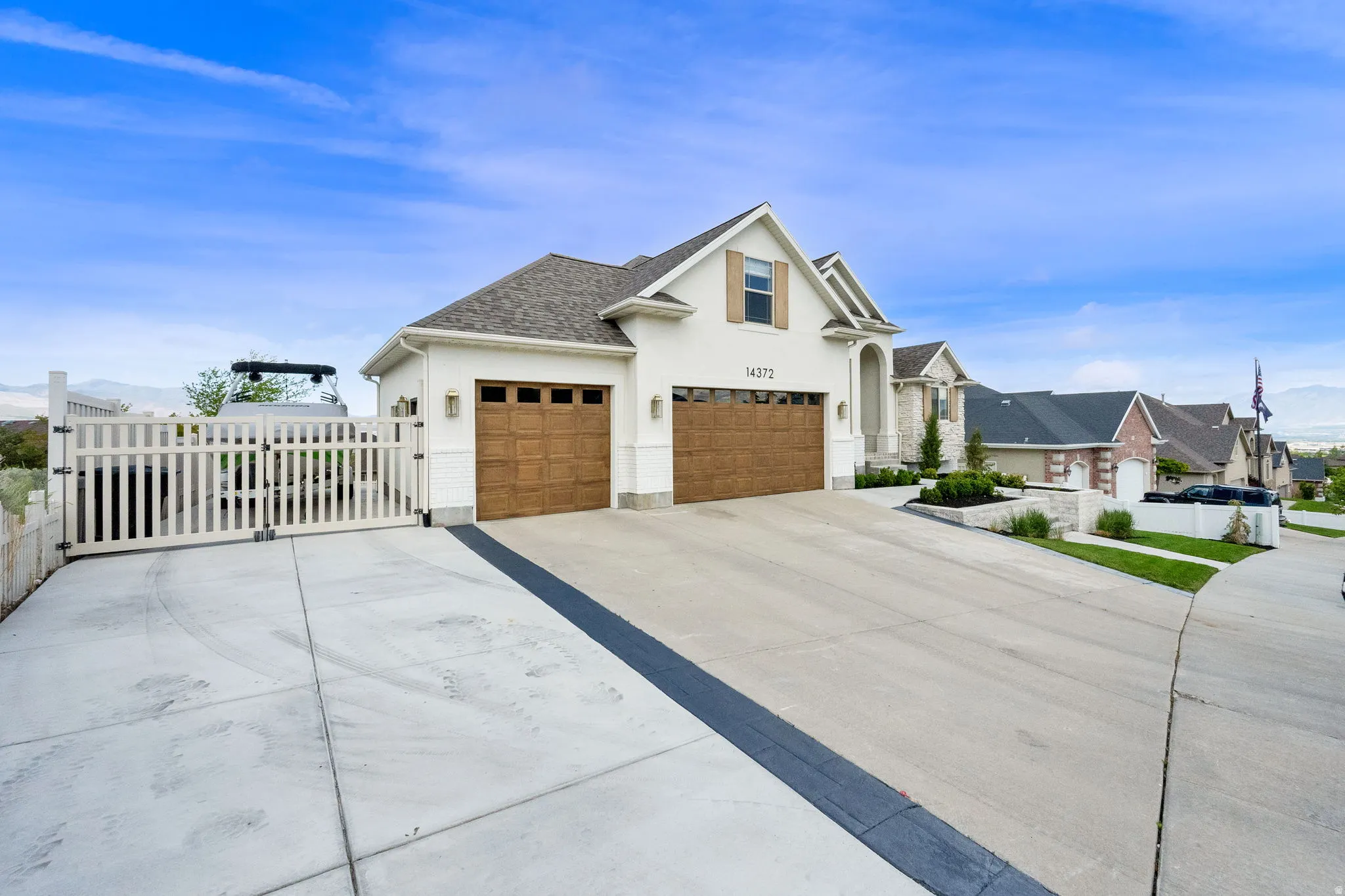 Contemporary residence featuring an attached two-car garage with wood-finish doors, a white picket fence and gate, a concrete driveway, and an elevated landscaping bed with stone retaining walls