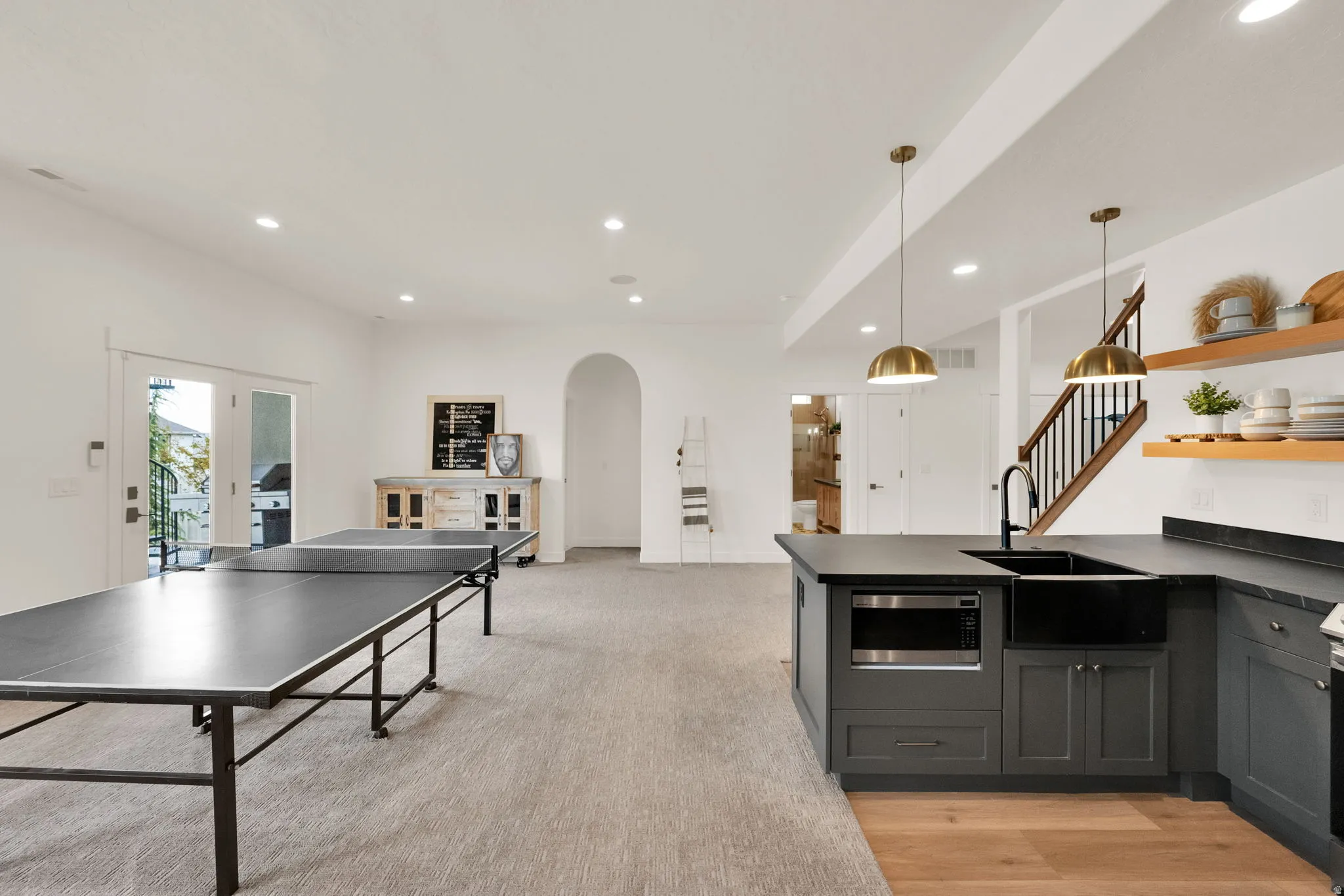 Spacious lower-level area featuring a full kitchen with dark cabinetry, integrated microwave, and large farmhouse-style sink
