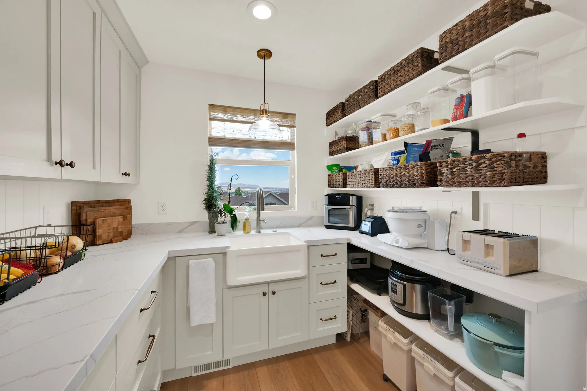 Spacious kitchen pantry featuring open shelving, white cabinetry, integrated farmhouse sink, marbled countertops, and wood-finish flooring