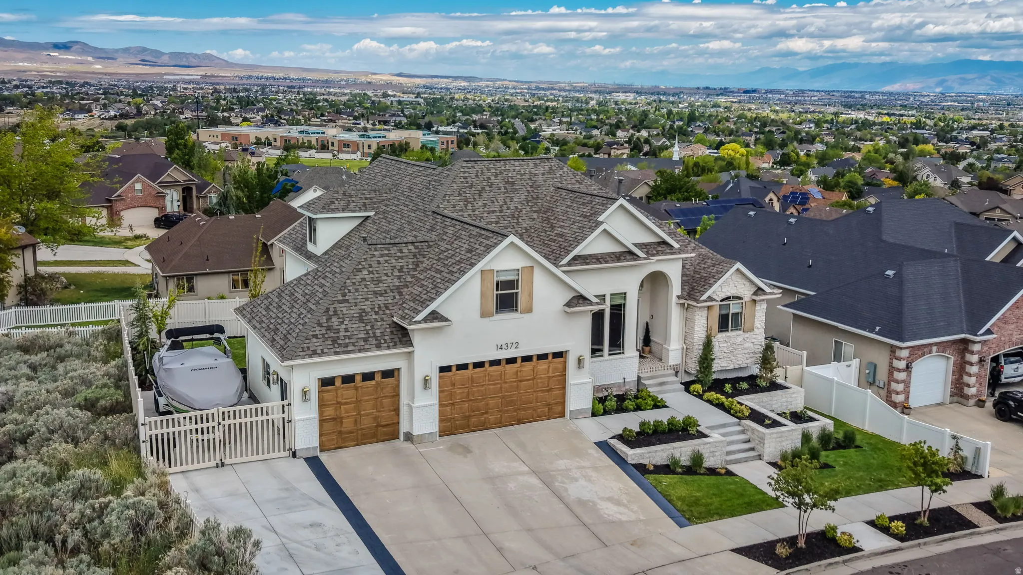 Contemporary stucco and stone exterior featuring a multi-gabled roofline, three-car garage with wood-finish doors, and a terraced front yard with integrated landscaping