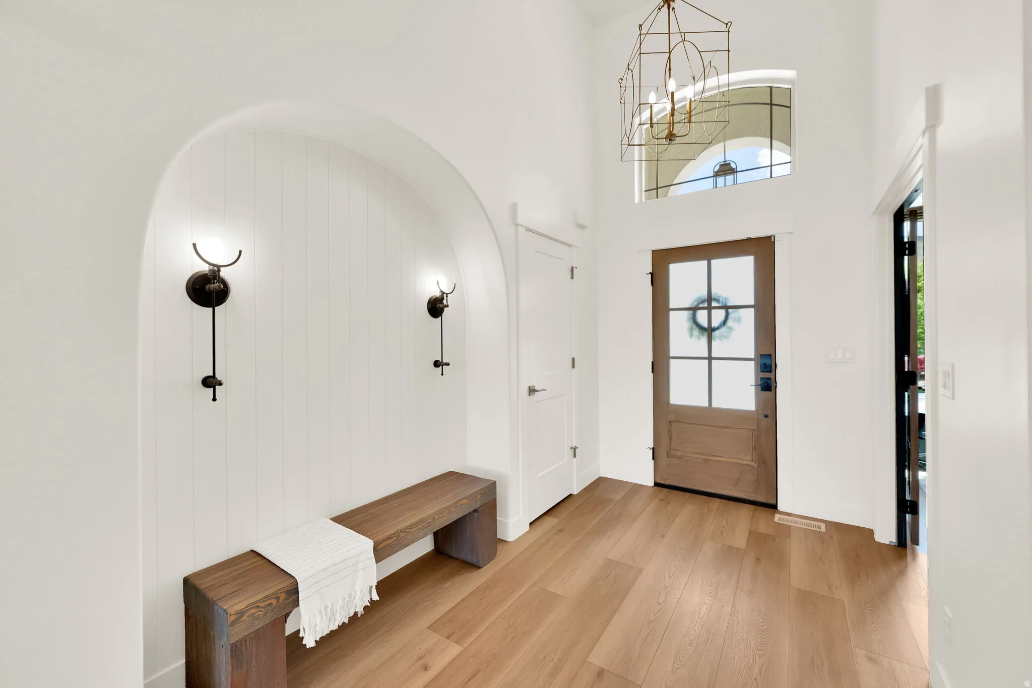Grand entry featuring a light wood door with glass panes, a geometric chandelier, and an arched alcove