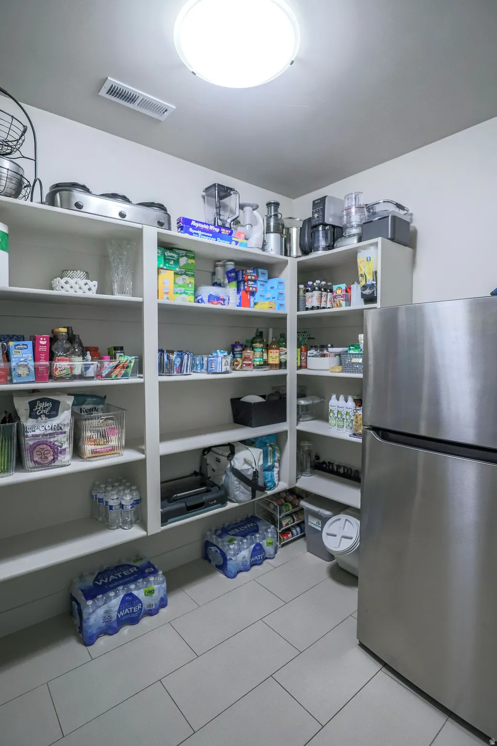 Corner pantry featuring built-in white shelving, recessed lighting, and light-toned rectangular tile flooring