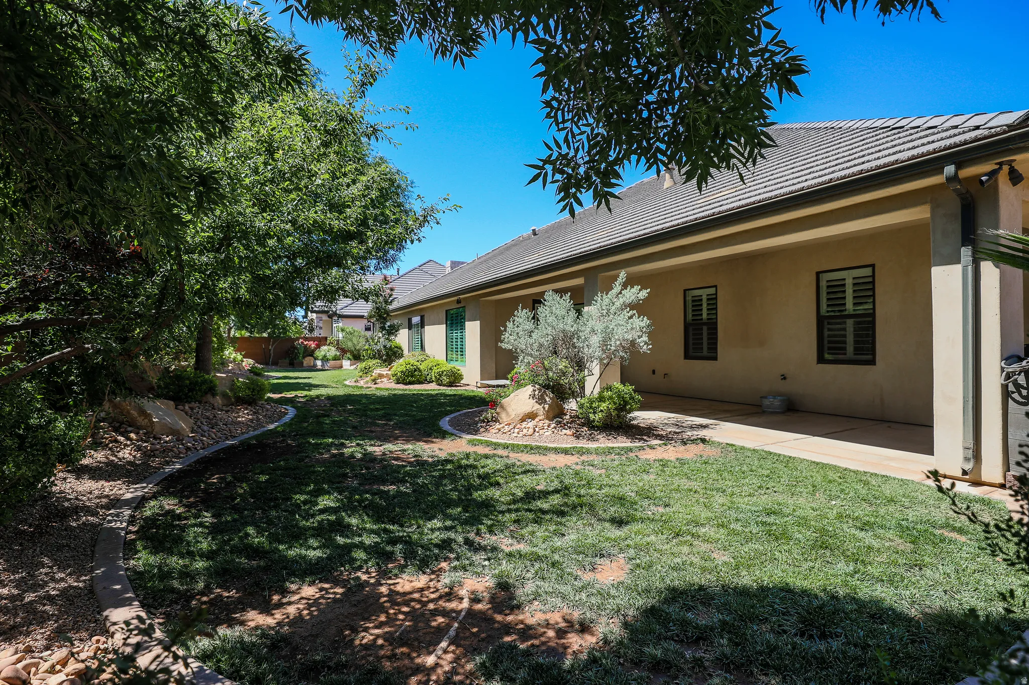 Expansive backyard featuring a manicured lawn, established trees, and a covered patio