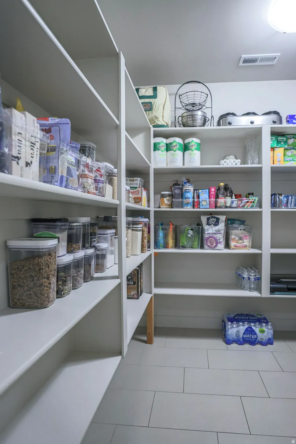 Walk-in pantry featuring extensive built-in shelving, light-toned walls, and large format floor tiling