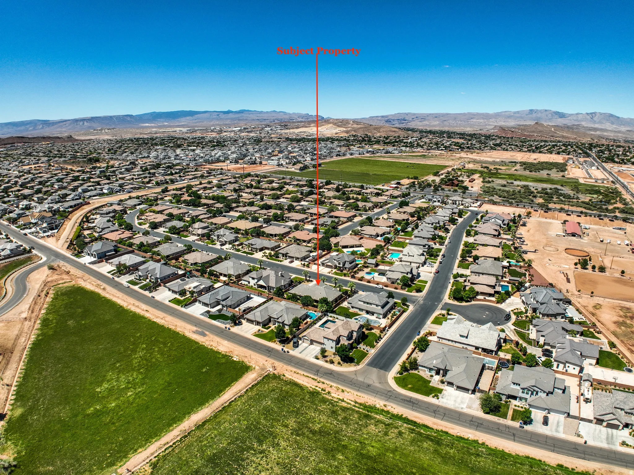 Aerial neighborhood perspective with extensive residential development, surrounding open green spaces, and distant mountain ranges